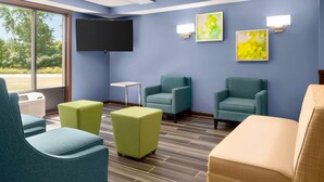 A modern waiting area with teal and yellow chairs, a flat-screen TV, and artwork on the walls. - Days Inn & Suites by Wyndham Merrillville (Merrillville)