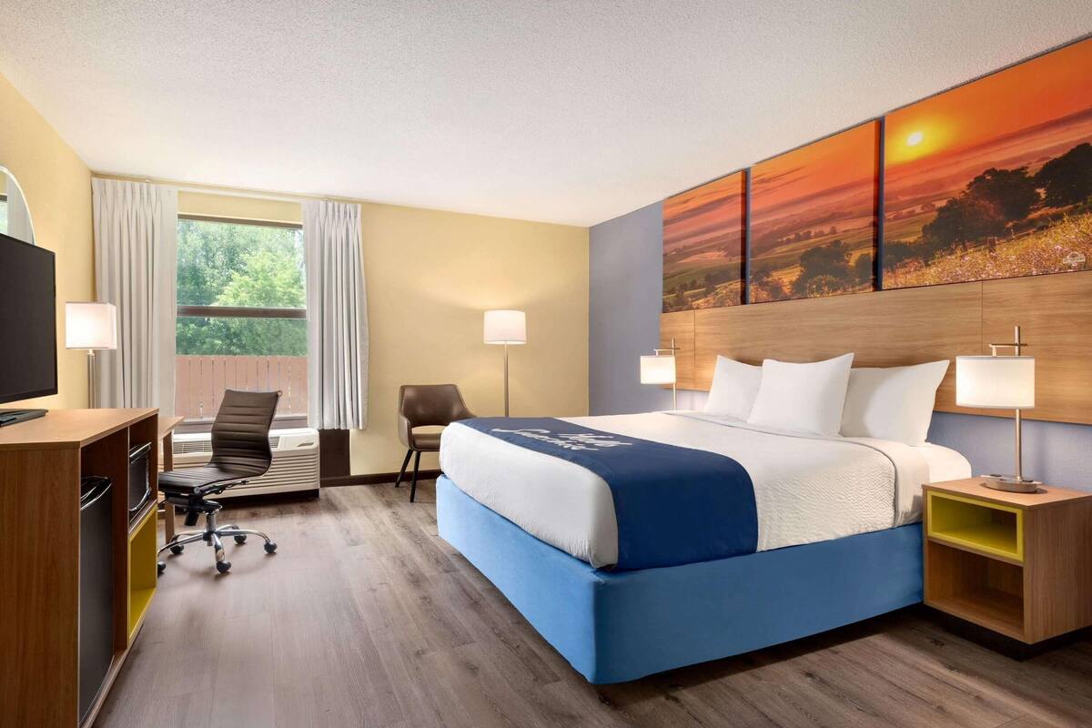 A hotel room with a bed, desk, chair, and a large painting on the wall.