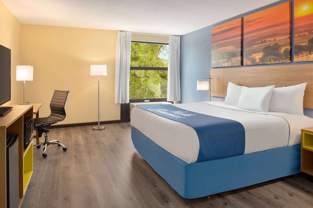 A hotel room with a bed, desk, chair, and a large window with curtains.
