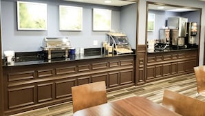A hotel breakfast area with a counter, coffee machines, and seating. - Days Inn & Suites by Wyndham Merrillville (Merrillville)