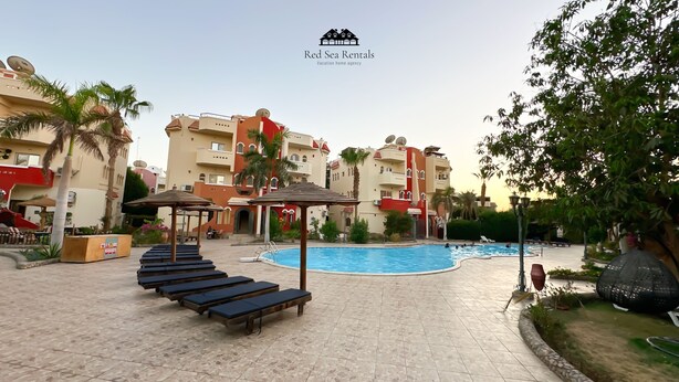 Een resort met een zwembad, ligbedden en een pergola.