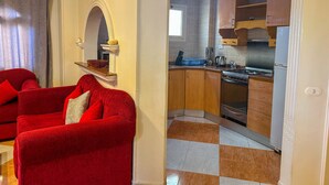 Een rode bank in een woonruimte met een geruite vloer, leidend naar een keuken met houten kastjes en een fornuis.