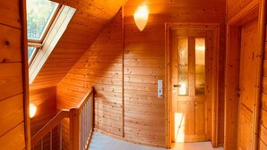 Un interior de madera con techo inclinado, una escalera y una puerta que da a otra habitación.