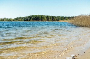 Un lago tranquilo con aguas cristalinas, una playa de arena y una orilla boscosa.
