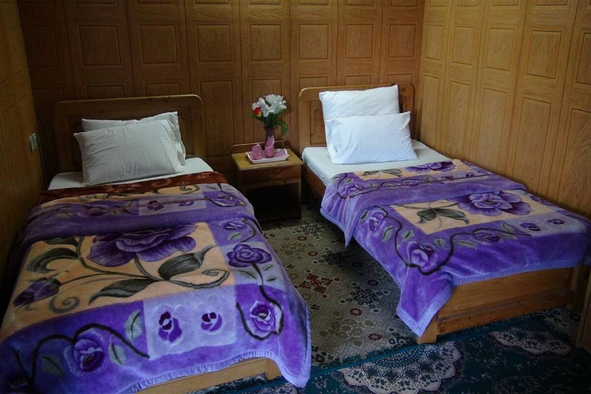 Two single beds with floral bedspreads, wooden headboards, and a nightstand with a vase of flowers between them.