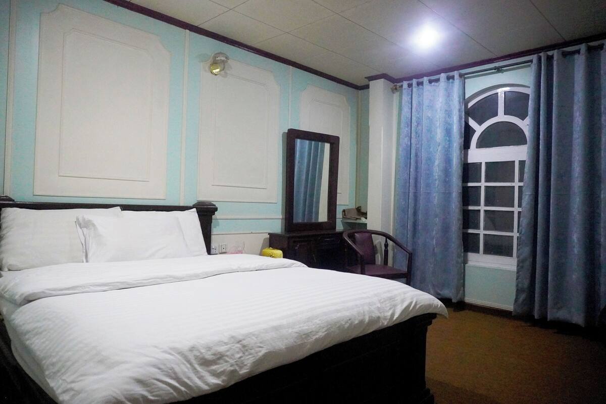 A bedroom with a bed, a dresser, a mirror, and a window with curtains.