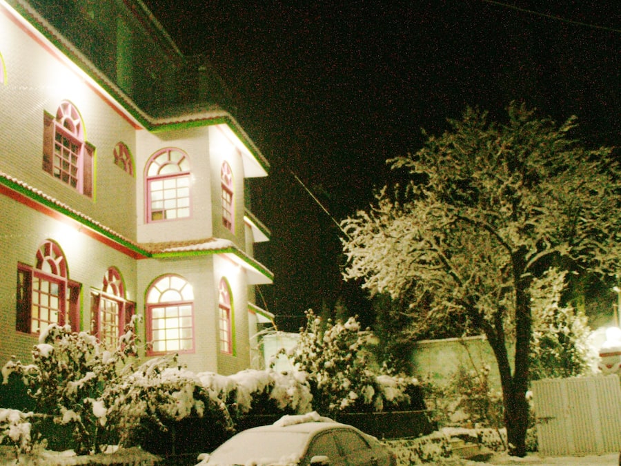 Una casa cubierta de nieve con un coche estacionado adelante, iluminada por luces exteriores.