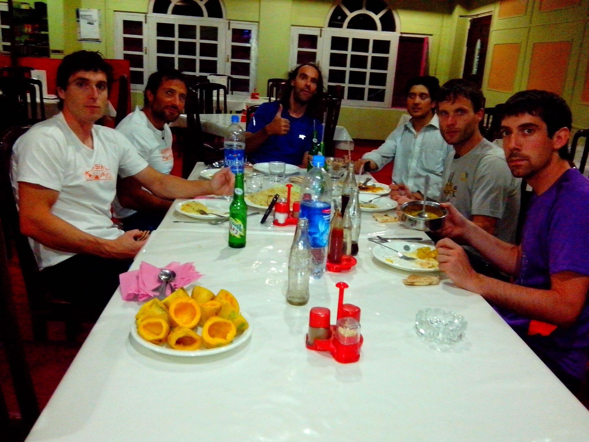 A group of people seated around a table with plates of food, bottles, and glasses.