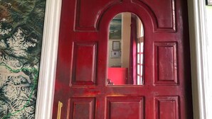 Una habitación con una calavera de carnero montada en la pared, una puerta roja y un cuadro con un paisaje colgado sobre la puerta.