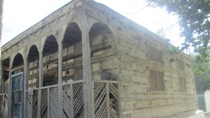 A rustic building with a wooden facade, multiple arched windows, and a blue door. - Hotel Dewanekhas (Skardu)