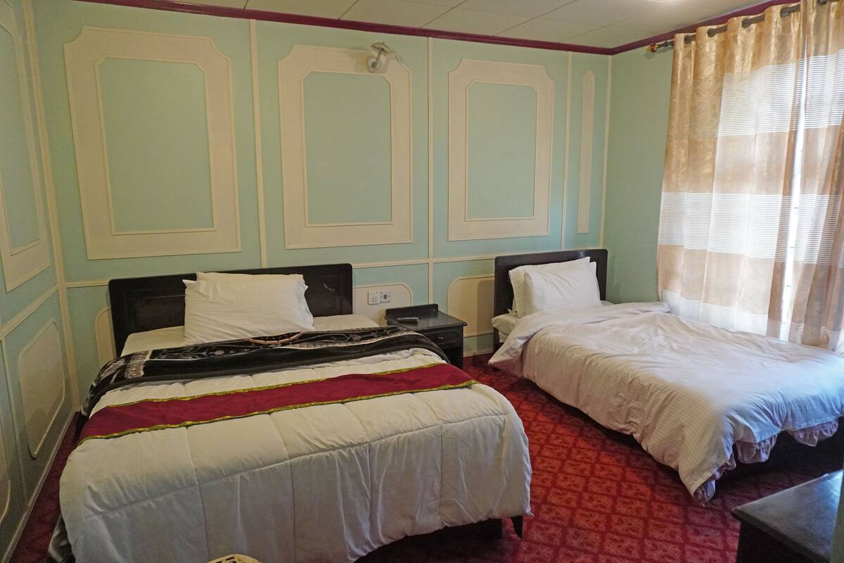 A hotel room with two beds, a red carpet, and a window with curtains.