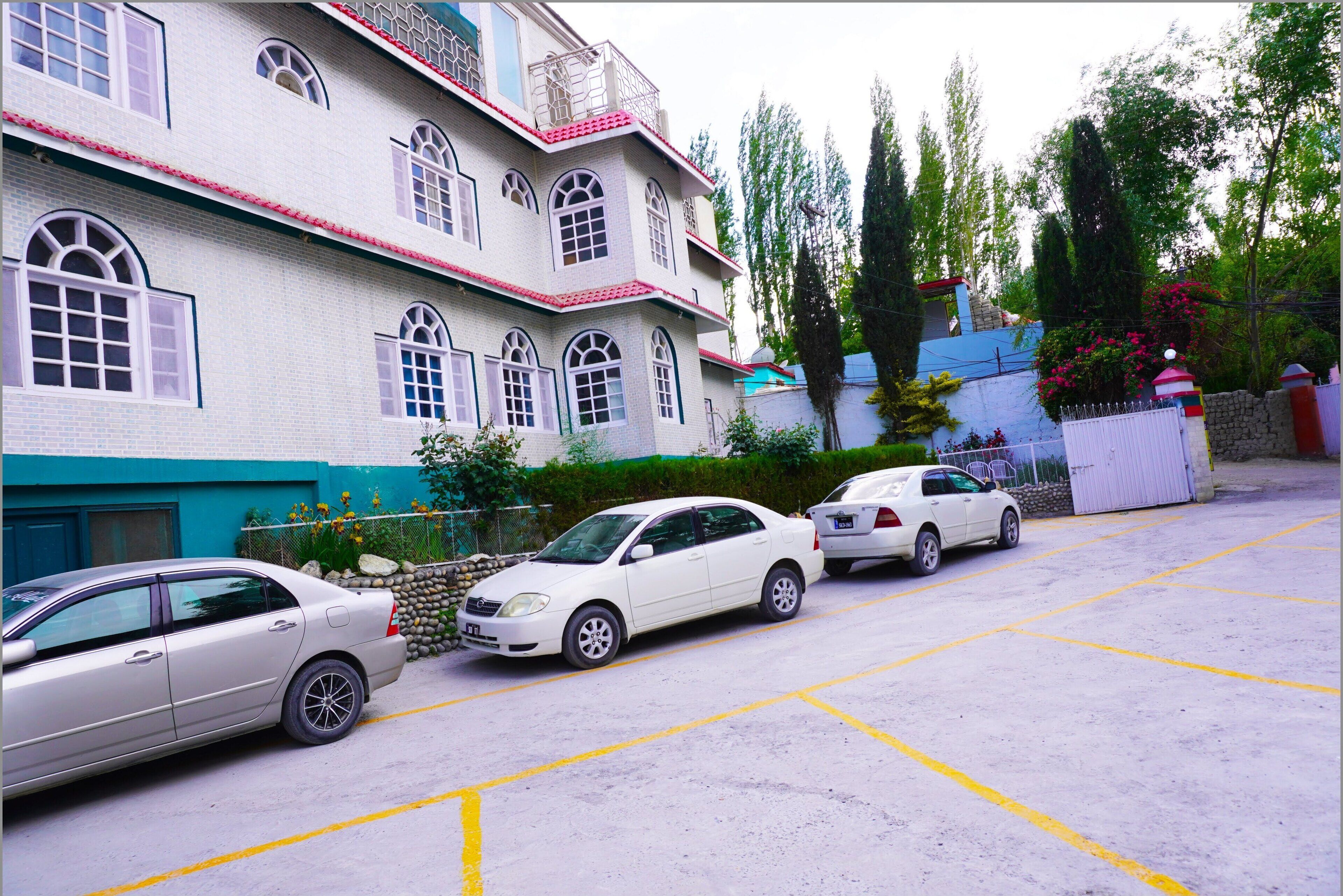 Un parking où sont garées trois voitures devant un immeuble doté de nombreuses fenêtres et d’un toit rouge.