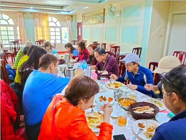 Un comedor con varias mesas y sillas, un ventilador y una ventana con cortinas.