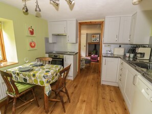 A compact kitchen with white cabinets, a dining table with a fruit-patterned tablecloth, and a wooden floor.