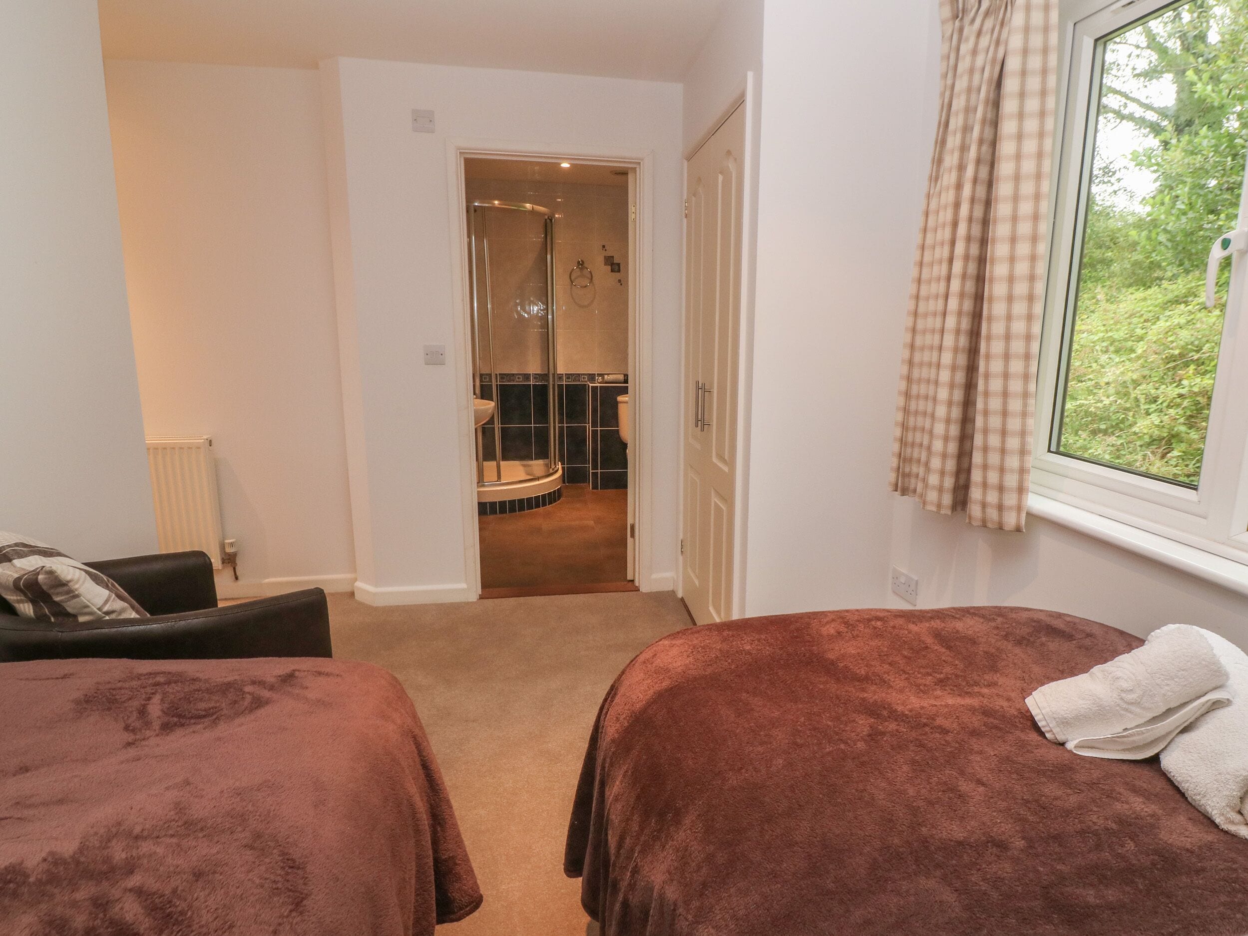 Een kamer met twee bedden, een raam met gordijnen, een radiator en uitzicht op een badkamer.