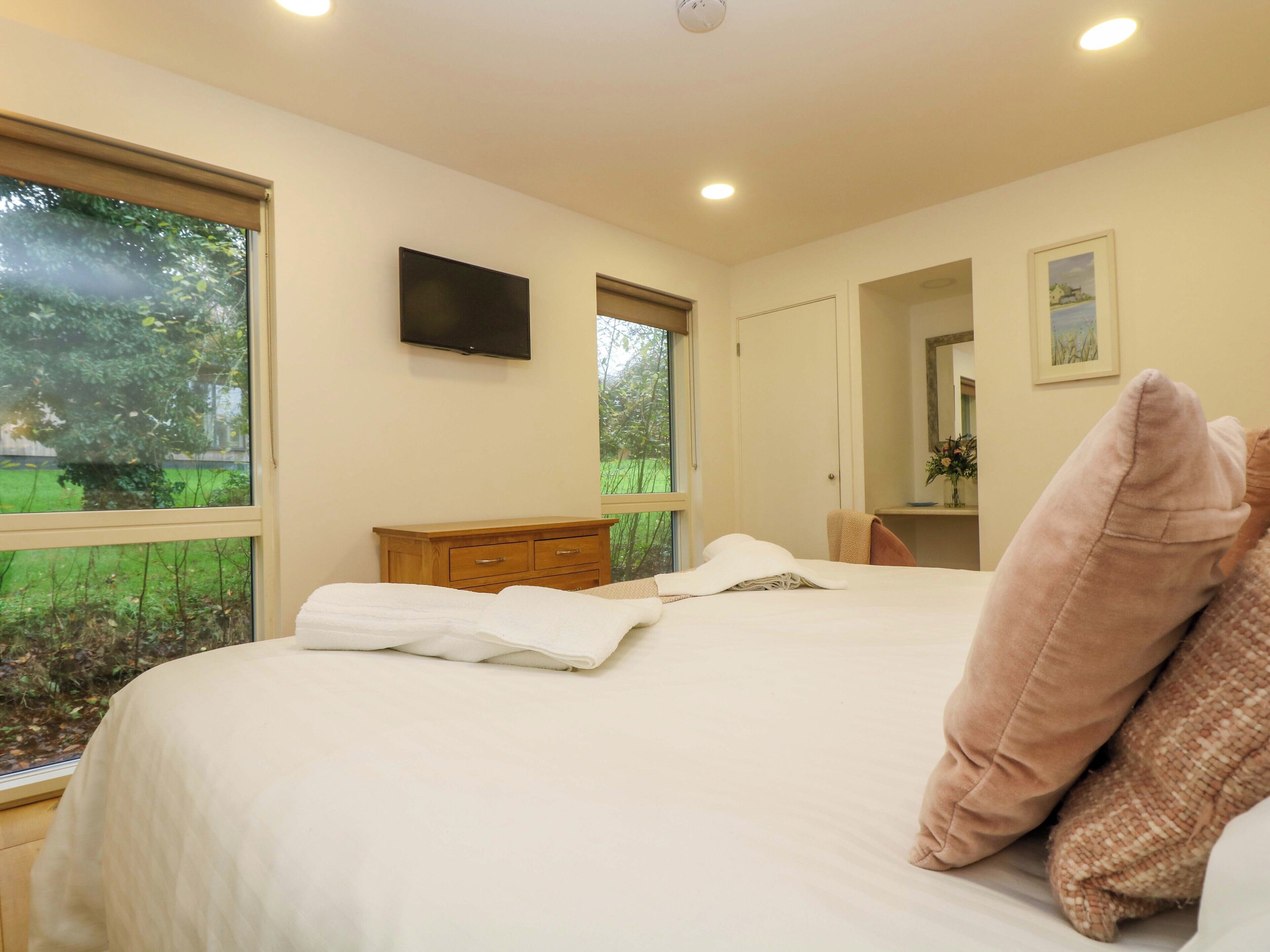 Un dormitorio con cama, televisor, cómoda y ventana con vistas a la vegetación.