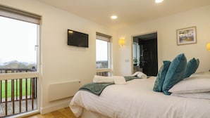 A bedroom with a bed, a TV, a window, and a balcony. - Juniper (Truro)
