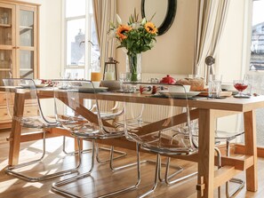 A dining area with a wooden table, clear glass chairs, and a vase with flowers. - Seion Chapel (Beaumaris)