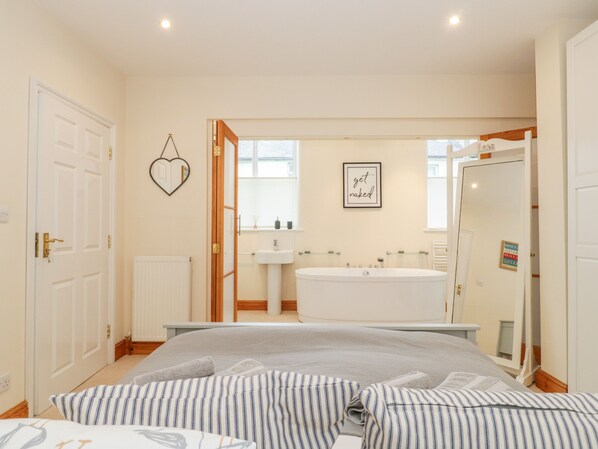A modern bedroom with a large bed, a built-in bathtub, and a separate shower area. - Seion Chapel (Beaumaris)