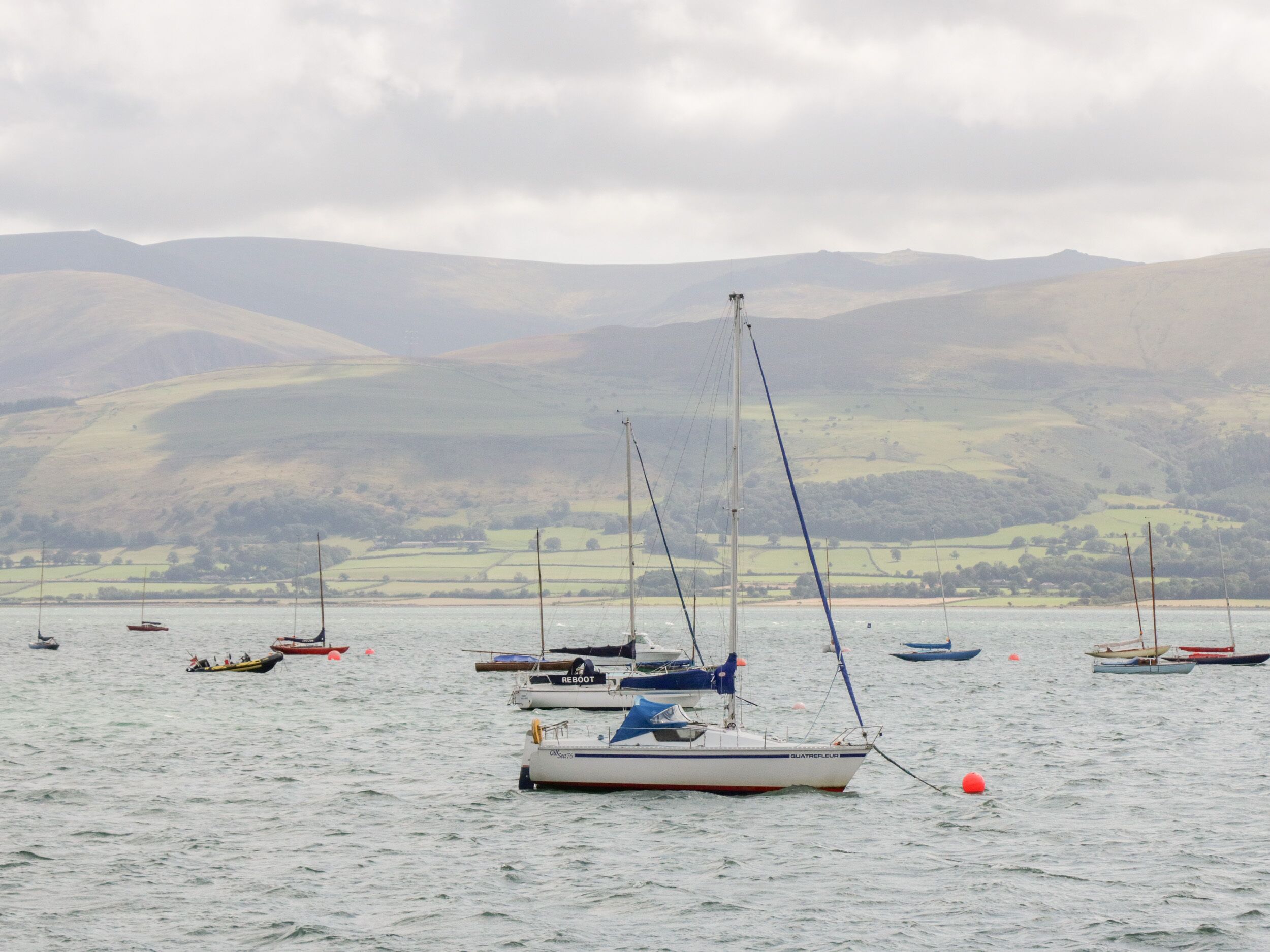 A calm body of water with several boats, including sailboats and motorboats, anchored or floating.