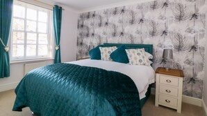 A bedroom with a bed, a nightstand, a lamp, and a window with curtains.