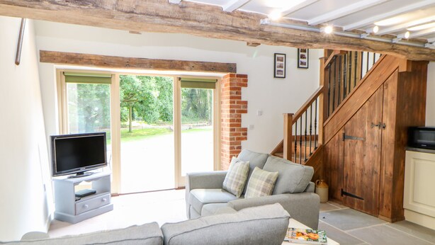 A living room with a grey sofa, a television, and a staircase leading to a loft. - The Cart Shed (Dereham)