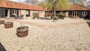 A courtyard with a gravel ground, two rustic wooden buildings with tiled roofs, outdoor seating, and potted plants. - The Cart Shed (Dereham)