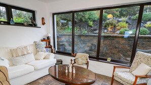 A cozy living room with a large window, a white sofa, a striped armchair, and a wooden coffee table. - Woodleigh Cottage (Ballycastle)