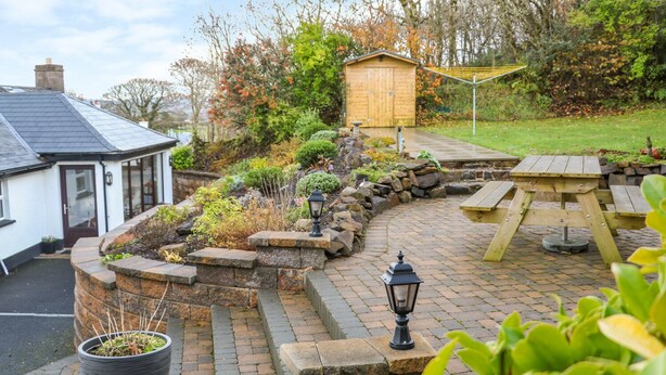 A garden patio with a wooden table and benches, a stone pathway, and a small wooden shed. - Woodleigh Cottage (Ballycastle)