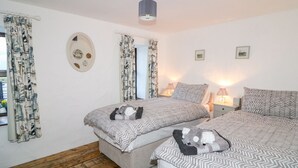 A bedroom with two beds, wooden flooring, and a ceiling light fixture. - Woodleigh Cottage (Ballycastle)