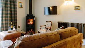 Un salon chaleureux avec une cheminée, un canapé, un fauteuil et un téléviseur fixé au mur.