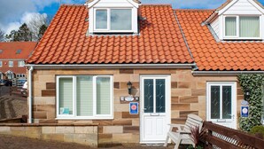 A two-story house with a red-tiled roof, stone facade, and a white door with a glass window. - Estuary View (Whitby)