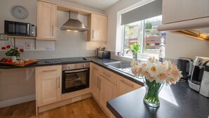 A modern kitchen with wooden cabinets, a built-in oven, a microwave, and a sink. - Estuary View (Whitby)