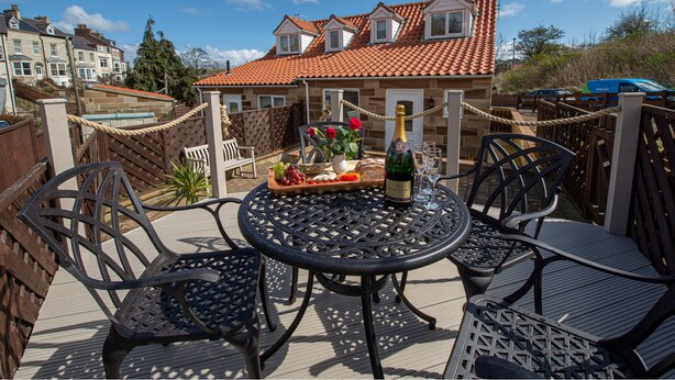 A patio with a round table, chairs, and a bottle of wine. - Estuary View (Whitby)