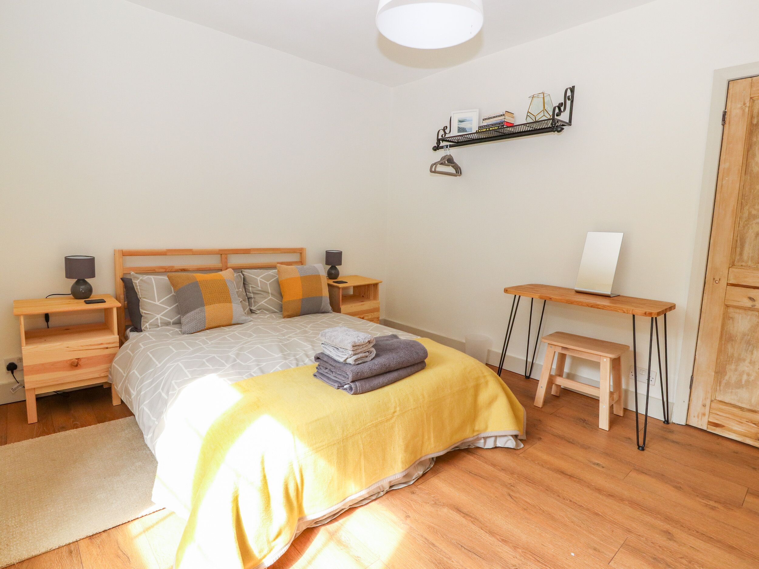 A bedroom with a bed, bedside tables, a desk, a chair, and a shelf with books and decorative items.
