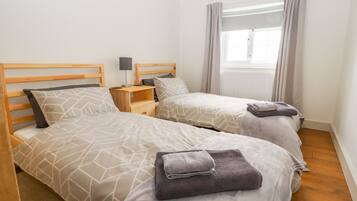 Habitación doble con dos camas, cada una con cabecero de madera, mesita de noche con lámpara y ventana con cortinas.