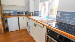 A compact kitchen with a washing machine, microwave, and oven. - Well House Farm Flat 1 (Chester)