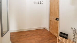 A room with wooden flooring, a wooden door, and a wall-mounted coat rack with hooks. - Well House Farm Flat 1 (Chester)