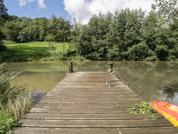 A wooden dock extending into a calm lake, surrounded by lush greenery and trees. - Primrose (Shepton Mallet)