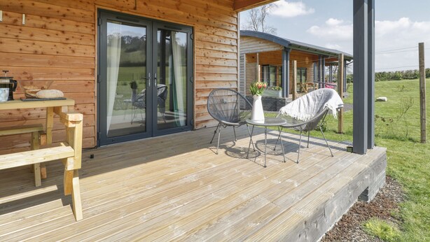 A wooden cabin with a covered porch, a dining table, and outdoor seating. - Primrose (Shepton Mallet)