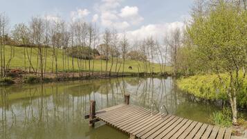 A wooden dock extending over a calm pond, surrounded by grassy hills and trees.