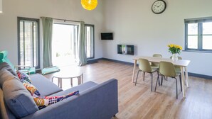 A modern living room with a sofa, dining table, chairs, a TV, and a clock on the wall. - Primrose (Shepton Mallet)