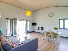 Una sala de estar moderna con un sofá, una mesa de comedor, sillas, un televisor y un reloj en la pared.