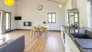 A modern kitchen with a curved ceiling, a dining area with a table and chairs, and a living room with a sofa. - Primrose (Shepton Mallet)
