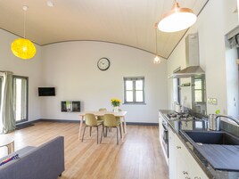 Una cocina moderna con techo curvo, un comedor con mesa y sillas, y una sala de estar con sofá.