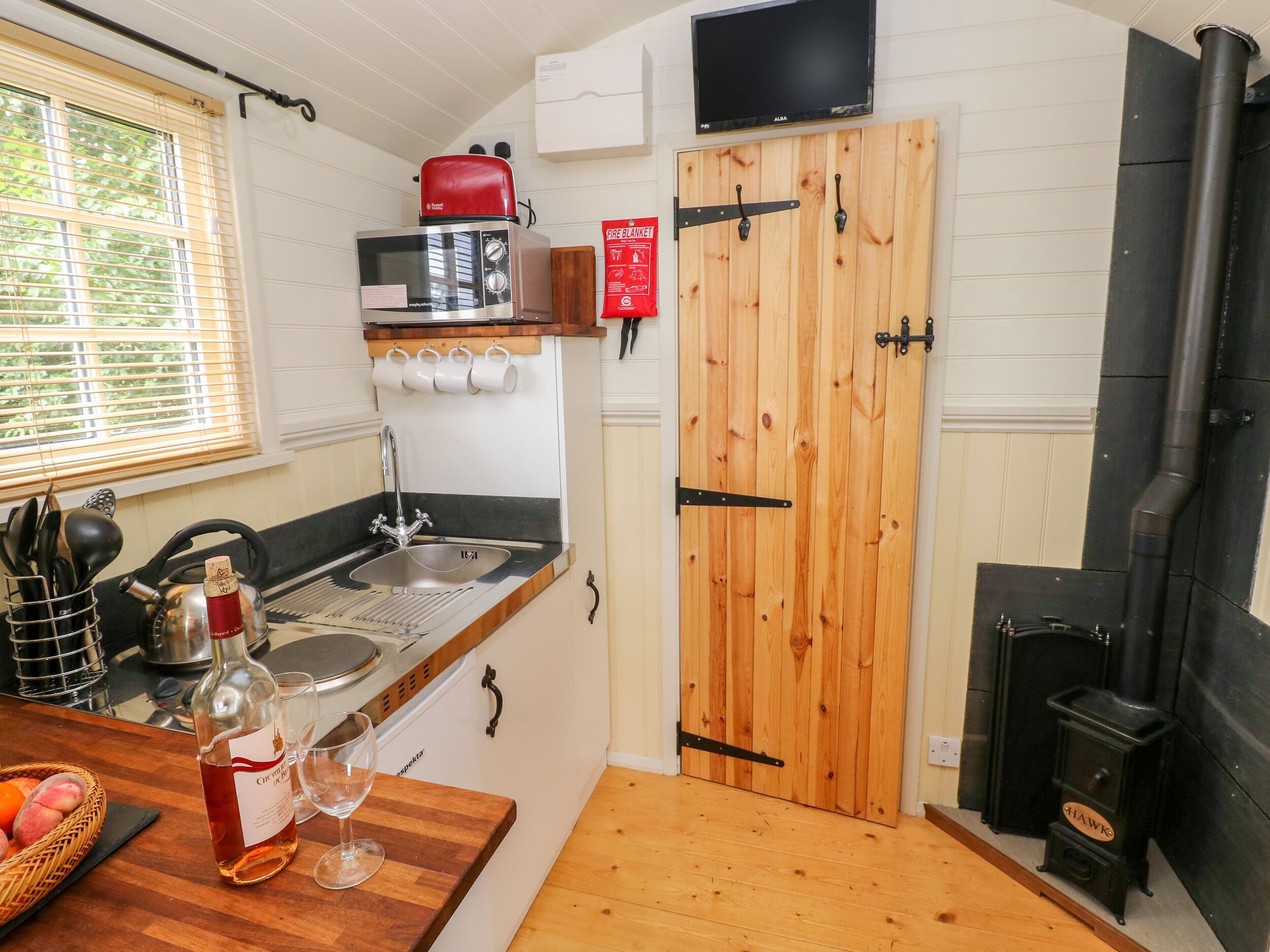 A compact kitchen with a wooden door, a built-in microwave, a sink, and a black stove.