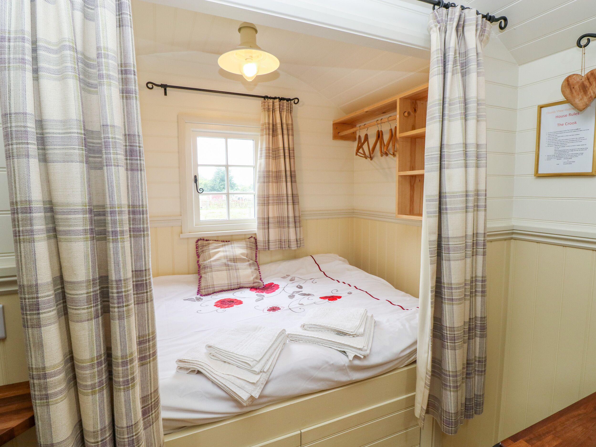 A bedroom with a bed, a window, a wooden shelf, and a heart-shaped decoration on the wall.