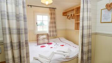 A bedroom with a bed, a window, a wooden shelf, and a heart-shaped decoration on the wall.