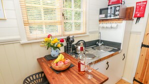 A compact kitchen with a wooden table, a sink, a microwave, and a fire blanket on the wall. - Shepherds Hut - The Crook (Milford Haven)