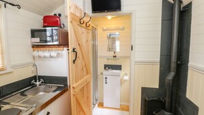 A compact kitchen with a sink, stove, and microwave. - Shepherds Hut - The Crook (Milford Haven)